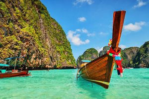 Long tail wooden boat at Maya Bay on Ko Phi Phi Le, made famous by the movie titled "The Beach". Beautiful cloudscape over the turquoise water and green rocks in Maya Bay, Phi Phi Islands, Thailand.