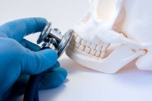 Diagnosis and detection of diseases of teeth in dentistry,disease of bones of face, upper and lower jaws, oral and maxillofacial surgery concept photo. Doctor hold in hand stethoscope on skull teeth